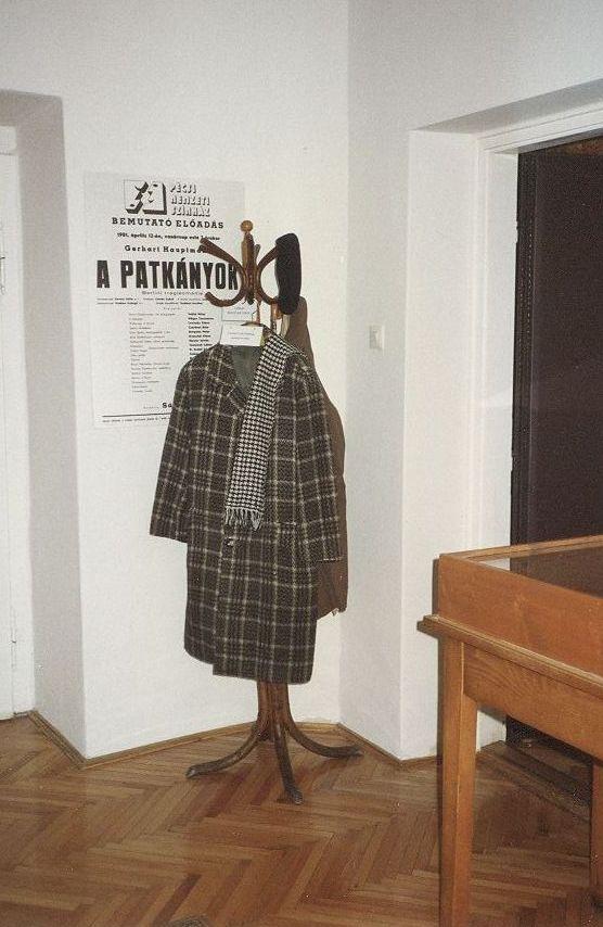 1997. Az 1996-ban a Csorba Győző Megyei Könyvtárban megnyitott Csorba Győző Emlékszoba részlete, Csorba kabátjával, sáljával, sapkájával. A háttérben a falon a Pécsi Nemzeti Színházban 1982-ben Csorba fordításában bemutatott Hauptmann-mű plakátja. (A